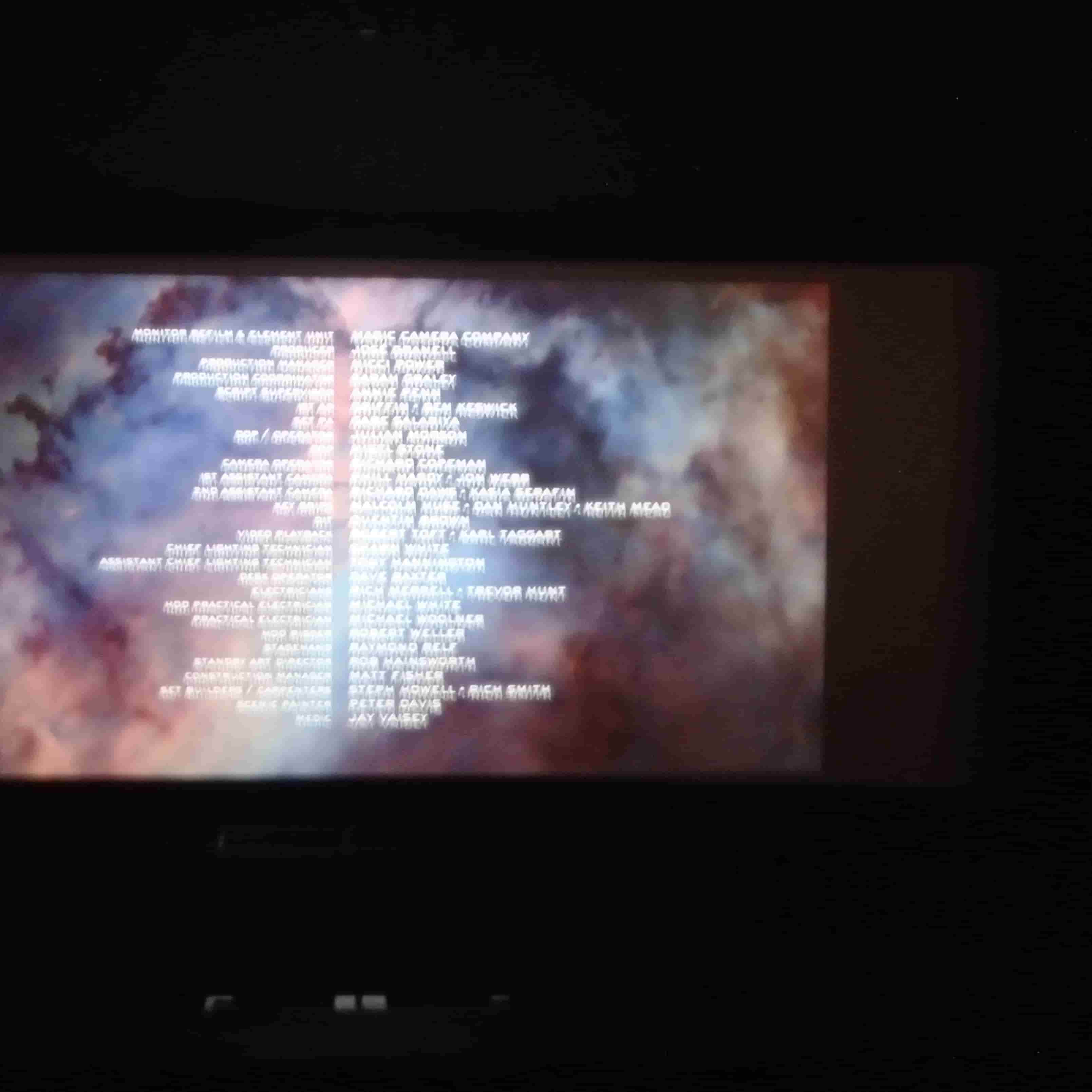 a blurry picture of end credits with a space background on a large screen in a dark theatre